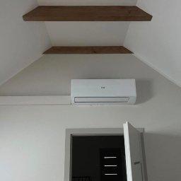 Cooling Service Łukasz Zawiłowicz - Biały klimatyzator Haier zamontowany na ścianie w pokoju z drewnianymi belkami stropowymi i otwartymi drzwiami. Minimalistyczny design wnętrza.