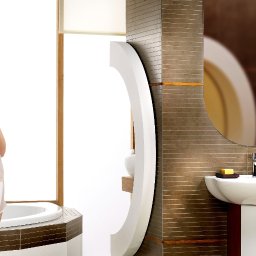 Szelest - Kobieta w satynowej bieliźnie w nowoczesnej łazience z owalnym lustrem, umywalką na postumencie i brązowymi płytkami.