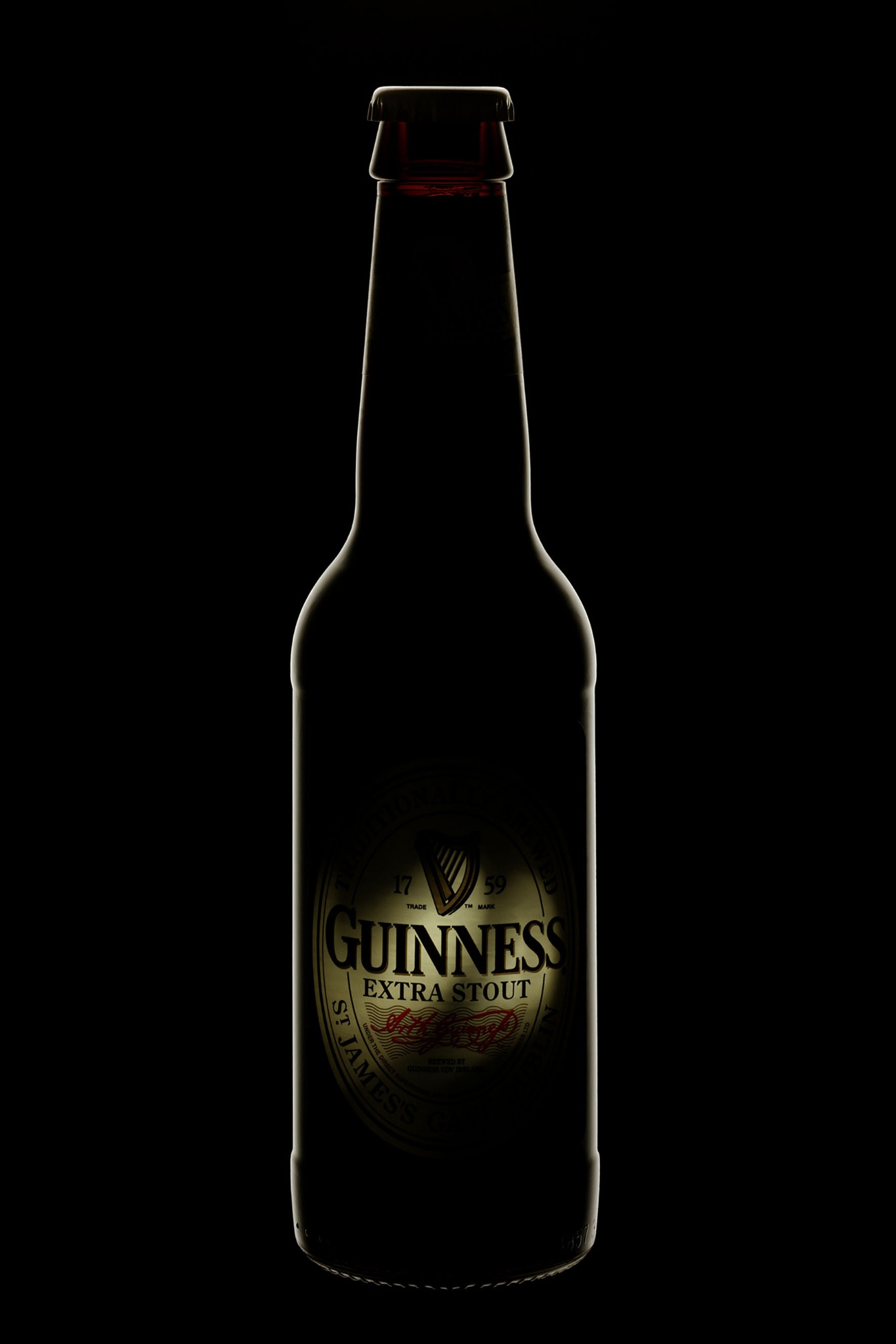 Butelka Guinness Extra Stout podświetlona na czarnym tle, eksponująca etykietę z logo i nazwą marki.