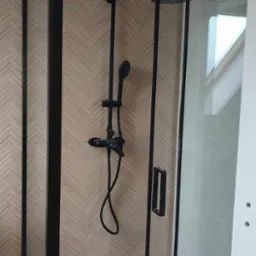 Nowoczesna kabina prysznicowa z czarnymi ramami i armaturą, ściana wykończona w geometryczny wzór jodełki.