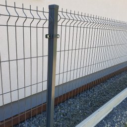 WILCZYŃSKI OGRODZENIA - Grafitowy panel ogrodzeniowy z podmurówką betonową, widok z bliska na słupki i wypełnienie, szara elewacja budynku w tle.