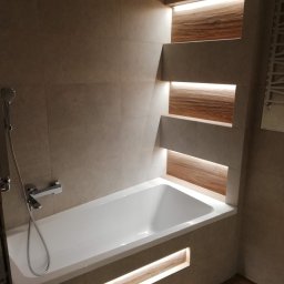 Jakub Naganowski - Nowoczesna łazienka z wanną w zabudowie, podświetlane wnęki z drewnianym akcentem i beżowe płytki. Minimalistyczny design z chromowaną armaturą.