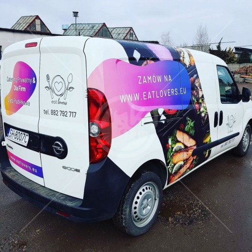 Okolicznościowe oklejenie firmowego samochodu dostawczego z grafiką dań i adresem strony internetowej cateringowej firmy.