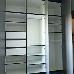 GaMeb - Otwarta, nowoczesna szafa wnękowa z szarymi drzwiami i białymi półkami, widoczne szuflady i drążek na ubrania. Minimalistyczny design, jasne wnętrze.