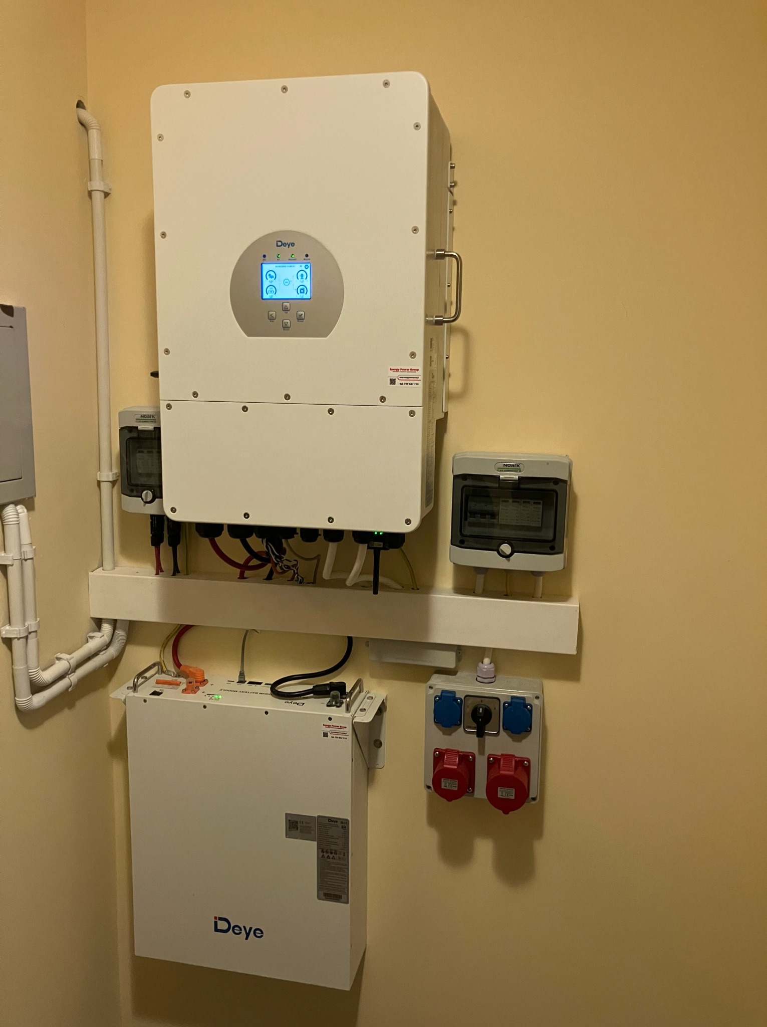 Zamontowany inwerter i bateria Deye na ścianie w pomieszczeniu. Widoczne przewody, zabezpieczenia i gniazda. Instalacja fotowoltaiczna wewnątrz budynku.