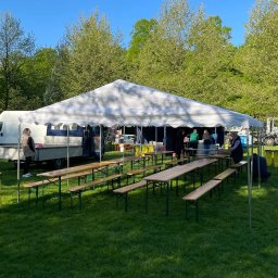 All4events - Biały namiot plenerowy z drewnianymi ławami i stołami na trawie, przygotowany na imprezę. W tle zaparkowany biały bus i zielone drzewa w słoneczny dzień.