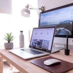 LK Project Łukasz Kamiński - Jasne biurko z laptopem wyświetlającym wykresy, monitor z górskim tłem, mysz, tablet graficzny i rośliny. Minimalistyczne, nowoczesne miejsce pracy.