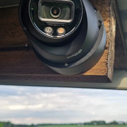 Go Sat Cam - Kamera Dahua zamontowana na drewnianej konstrukcji z widokiem na zielone pole i pochmurne niebo. Obudowa kamery w kolorze czarnym, widoczne diody IR.