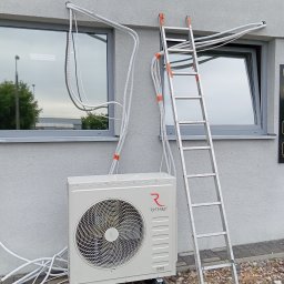 Klima Instalator - Biała jednostka zewnętrzna klimatyzacji Rotenso zamontowana na elewacji budynku, z widocznymi przewodami i drabiną opartą o ścianę. Instalacja w toku.