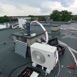 Klima Instalator - Montaż klimatyzacji GREE na dachu budynku z widocznymi narzędziami i przewodami. Instalacja w trakcie realizacji, pochmurne niebo w tle.