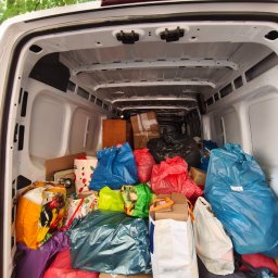 Usługi transportowe Bartłomiej Borowczyk - Wnętrze białej furgonetki załadowane po sam dach różnokolorowymi workami foliowymi i kartonowymi pudłami, w tym torbą z logo 'ACTION', ciasno ułożonymi. U góry widać zielone liście drzew.