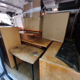 Usługi transportowe Bartłomiej Borowczyk - Wnętrze białego busa dostawczego, z widocznym drewnianym krzesłem o czarnych nogach, elementami mebli i zaklejonymi kartonami, przygotowane do transportu.