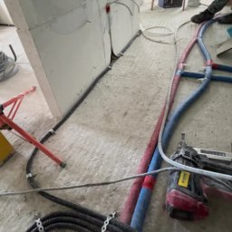 Belweder Energy - Wnętrze w trakcie prac: widoczne kable elektryczne przymocowane do ściany, rury w izolacji oraz narzędzie do mocowania. Na podłodze widoczny żółty element mocujący.