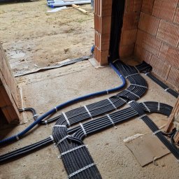 Belweder Energy - Ułożone na betonowej posadzce czarne peszle z przewodami, spięte metalowymi opaskami, oraz niebieski peszel, prowadzone do ścian z pustaków ceramicznych w trakcie budowy.