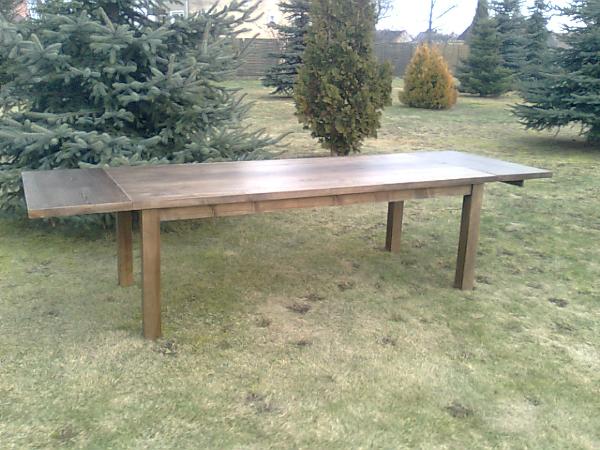 Rozkładany stół z drewna na trawie w Ziębicach, otoczony iglakami.