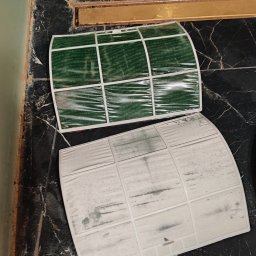 LokalnaEkipa - Dwa filtry klimatyzacji na ciemnym blacie: jeden brudny, szary od kurzu, drugi czysty, zielony i mokry po myciu, obok złotego odpływu.