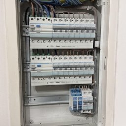 Jakub Śpiewak - Otwarta rozdzielnica elektryczna z precyzyjnie ułożonymi przewodami i zamontowanymi modułami zabezpieczającymi Hager, w tym wyłącznikami nadprądowymi i różnicowoprądowymi.