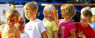 Grupa dzieci z pomalowanymi twarzami w motywy zwierzęce i superbohatera, stojących obok siebie podczas imprezy plenerowej.