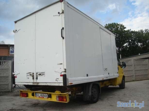 Żółto-biały samochód dostawczy z zabudową kontenerową, widok z tyłu, tablica rejestracyjna DL 46866, zaparkowany na placu.