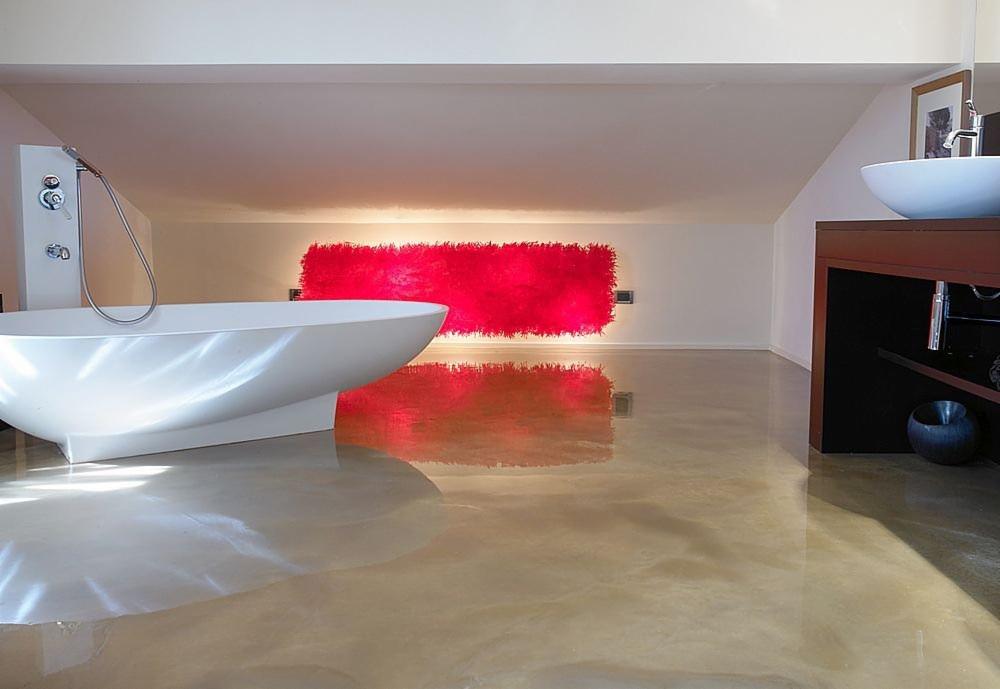 Błyszcząca, jasna podłoga epoksydowa w nowoczesnej łazience z wolnostojącą białą wanną i intensywnie czerwonym elementem dekoracyjnym na ścianie.
