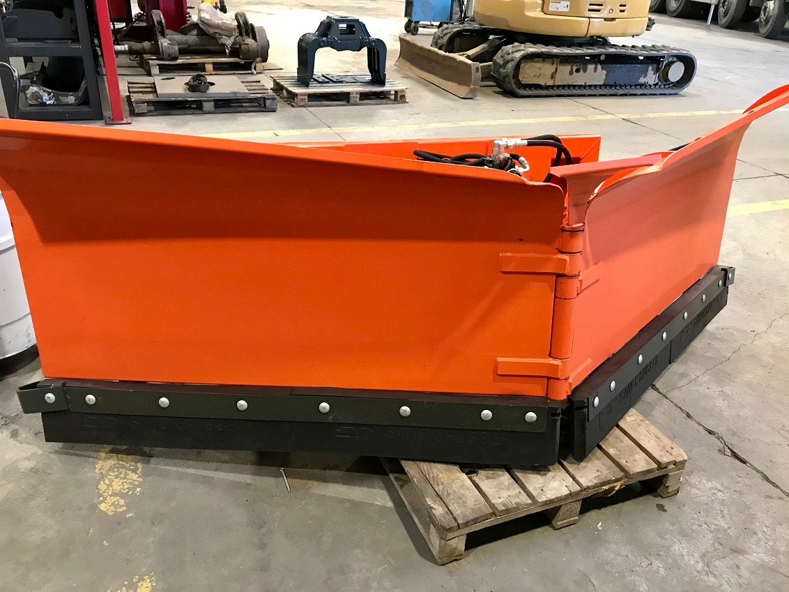 Pomarańczowy pług do odśnieżania, widok z boku, umieszczony na drewnianej palecie w hali.