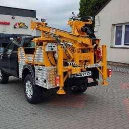 WM Geotechnika S.C. - Solidna, żółta wiertnica hydrauliczna Soltechnica zamontowana na czarnym pickupie, zaparkowanym na brukowanym placu przed budynkami.