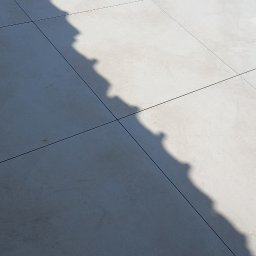 Katarzyna Hofman - Jasne, wielkoformatowe płytki tarasowe z wyraźnym cieniem o ząbkowanym kształcie. W tle fragment bruku i szary, ukośny element konstrukcyjny.
