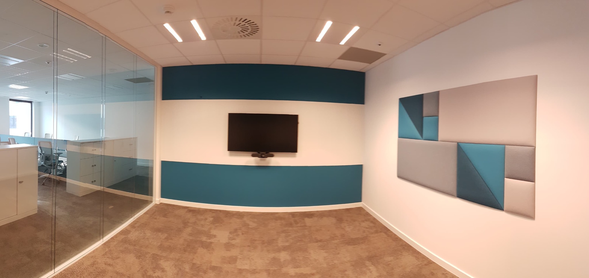 Nowoczesne wnętrze biura z przeszkloną ścianą, ścianą akcentową w pasy błękitu i bieli, telewizorem i dekoracyjnym panelem ściennym z geometrycznym wzorem w odcieniach szarości i błękitu.