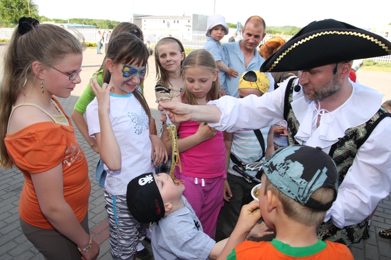 Mężczyzna przebrany za pirata karmi spaghetti grupę dzieci podczas zabawy na świeżym powietrzu, jedno dziecko ma pomalowaną twarz w motyle.