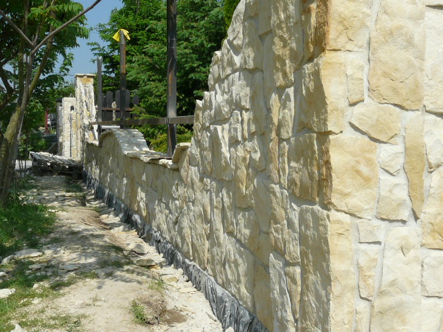 Fragment kamiennego ogrodzenia w trakcie budowy, widoczne elementy konstrukcyjne i podłoże, jasny kamień.