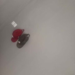 Mateusz Choczaj - Dwie czapki z daszkiem, czerwona i ciemnoszara, wiszące na gładkiej, jasnoszarej ścianie, z dwoma małymi białymi kwadratowymi elementami powyżej.