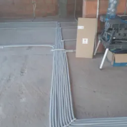 Instalacja elektryczna w peszlach ułożona na podłodze w surowym stanie w Teresinie, widoczne ściany z cegły i częściowo położone przewody.