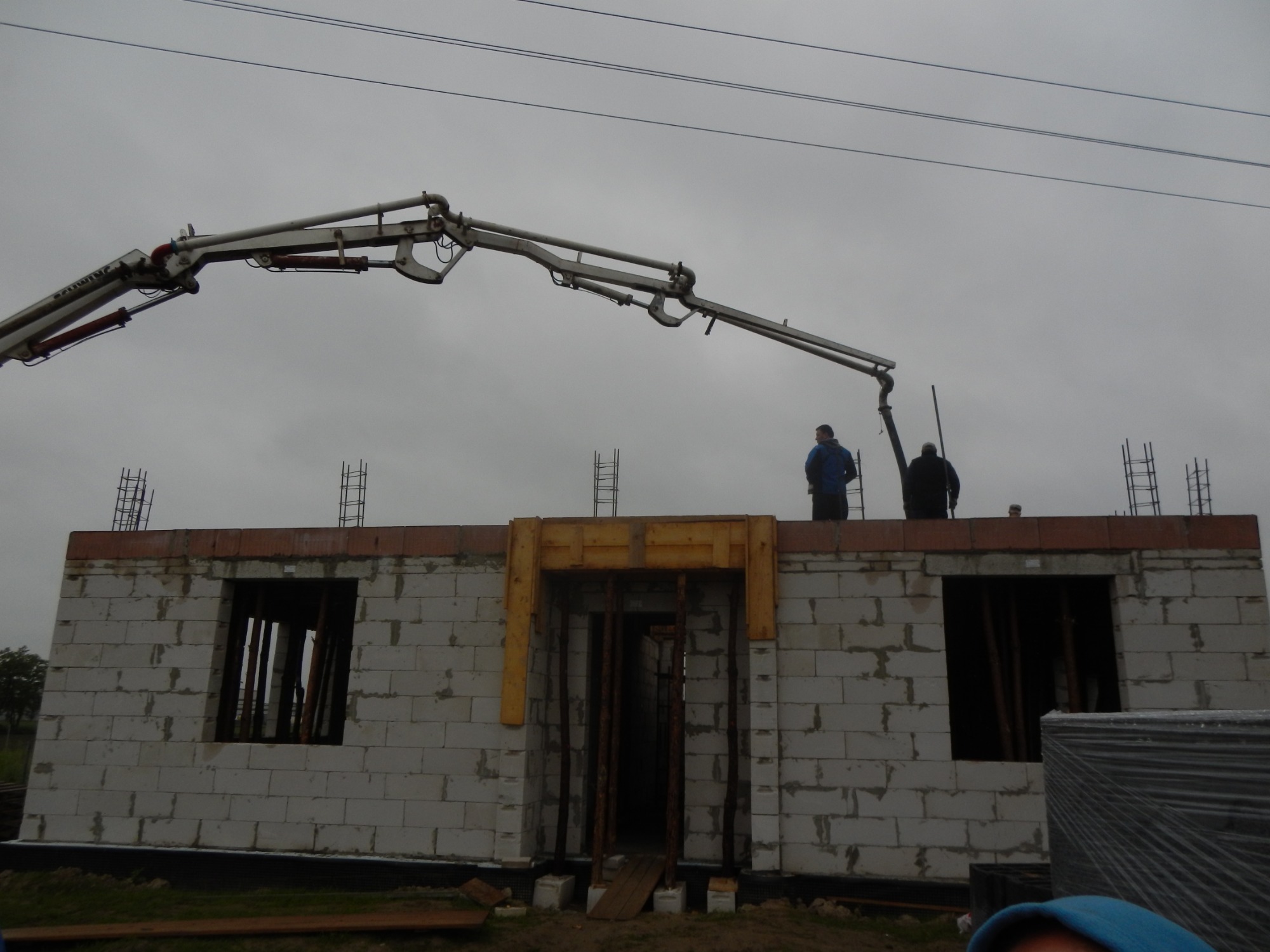 Budowa domu z betonu komórkowego: pracownicy obsługują pompę do wylewania betonu na strop, widoczne zbrojenia i szalunki okienne.