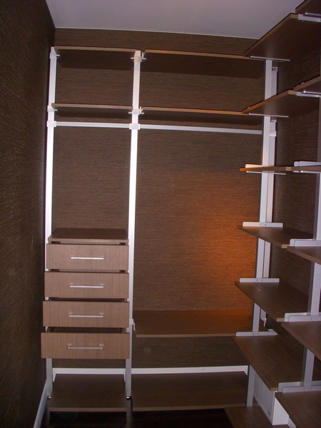 Wnętrze garderoby z systemem półek i szuflad w odcieniach brązu i bieli, na tle ściany o fakturze tapety.