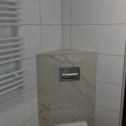 Przemek Rymer - Nowoczesna toaleta z podwieszaną miską WC i zabudowaną spłuczką wykończoną beżowymi płytkami imitującymi marmur. Biały grzejnik drabinkowy, jasne kafelki i drewnopodobna podłoga.