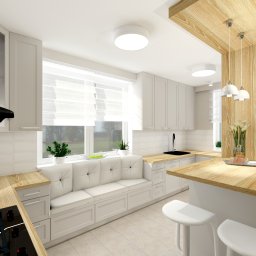 Befart Beata Nowacka - Jasna kuchnia z białymi szafkami, drewnianym blatem i siedziskiem pod oknem z widokiem na zieleń, uzupełniona o drewniany bar z wiszącymi lampami i roślinami doniczkowymi.