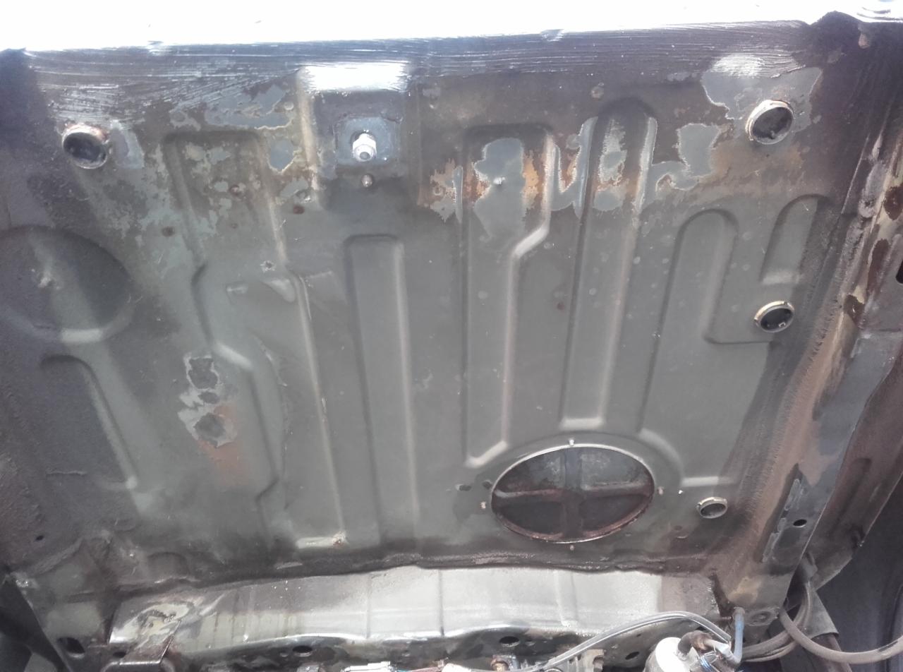 Podwozie samochodu z widocznymi śladami korozji i miejscami po naprawach blacharskich, widoczne otwory technologiczne i elementy konstrukcyjne.