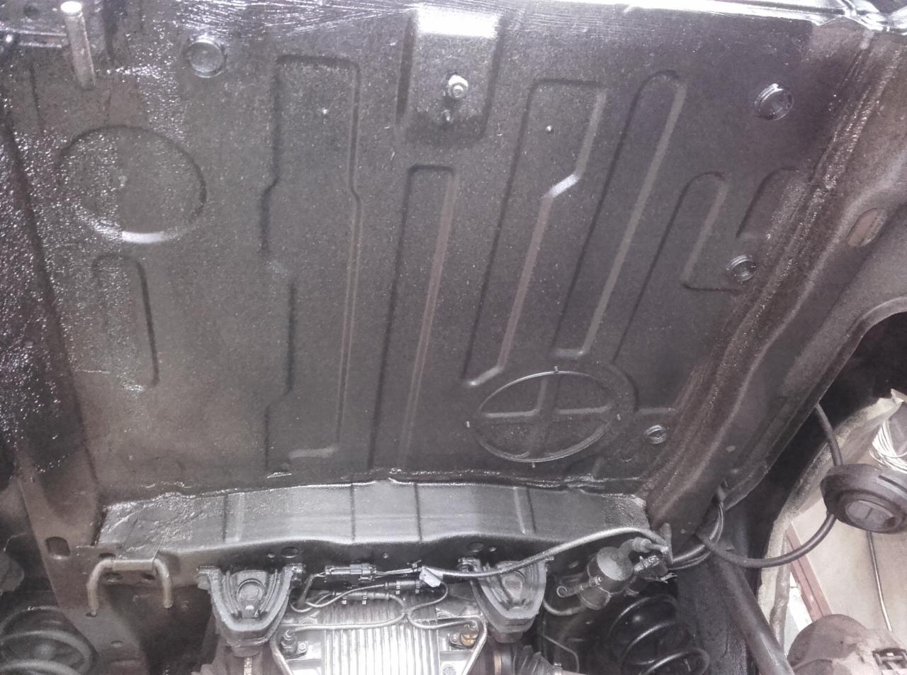 Spód samochodu po nałożeniu czarnej, ochronnej powłoki antykorozyjnej, widoczne elementy zawieszenia i podwozia.