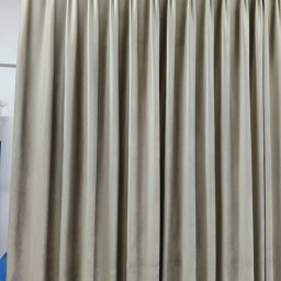 Wid-Art Studio Dekoracji Okien - Beżowa, gęsto plisowana zasłona z grubego, matowego materiału, zawieszona na srebrnym karniszu z kółkami. Widoczne eleganckie, równomierne fałdy tworzące klasyczny wygląd.