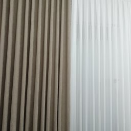 Wid-Art Studio Dekoracji Okien - Eleganckie, plisowane zasłony: beżowa, zaciemniająca obok białej, transparentnej firany, zawieszone na podwójnych szynach sufitowych.