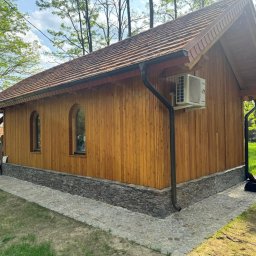 PPHU DREWMAR Zbigniew Jangas - Drewniany budynek z deskowanym wykończeniem, łukowymi oknami, kamienną podmurówką i brązowym dachem, otoczony brukowaną ścieżką i drzewami w słoneczny dzień.