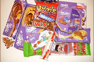 Różnorodny zestaw słodyczy: czekolady Milka, batoniki Snickers i Twix, cukierki Dumle, wafle i inne przysmaki ułożone na białym tle. Widoczne świąteczne pierniczki w kształcie choinek.