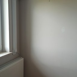 GPtermoinstal - Biała klimatyzacja typu split z wyświetlaczem '21' na jasnoszarej ścianie. Estetyczne maskowanie instalacji wzdłuż ściany i sufitu. W tle biały grzejnik pod oknem, panele podłogowe.