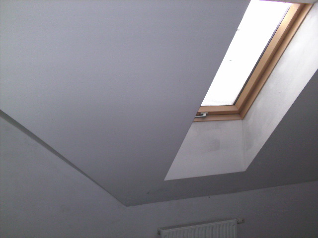 Wykończona poddaszowa przestrzeń z oknem dachowym i zabudową z płyt karton-gips, widoczny grzejnik pod oknem.