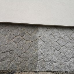 MICHAŁ GRACZYK - Kamienna podmurówka budynku z wyraźnym podziałem na brudną (lewa strona) i czystą (prawa strona) część po myciu, z jasnym tynkiem powyżej.