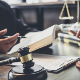 Kancelaria Radcy Prawnego Dorota Kurek -Zielińska - Prawnik w Wołominie podczas konsultacji, wskazujący na otwartą księgę prawa. Na biurku młotek sędziowski i waga Temidy, symbolizujące sprawiedliwość.