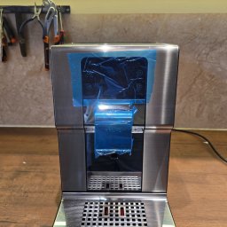 JaroHer Serwis - Nowy ekspres do kawy Krups Intuition ze szczotkowanej stali, z niebieską folią ochronną na panelu dotykowym, na drewnianym blacie, z narzędziami w tle.