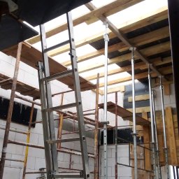 Zakład Remontowo Budowlany DOMEX Marek Krzak - Budowa domu z białych bloczków, widoczne metalowe stemple i drewniane szalunki pod strop. Na pierwszym planie aluminiowa drabina.