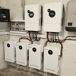 Elektrotechnika Konrad Wykowski - Zainstalowany system fotowoltaiczny z dwoma inwerterami SRNE i jednym Fronius Symo, połączony z czterema magazynami energii SRNE Lithium Battery Energy Storage, widoczny na tle betonowej ściany...