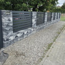 Prywatne - Nowoczesne ogrodzenie z ciemnoszarych poziomych przęseł, osadzone na betonowych słupkach i podmurówce z marmurkowym wzorem, obok żwirowej ścieżki.